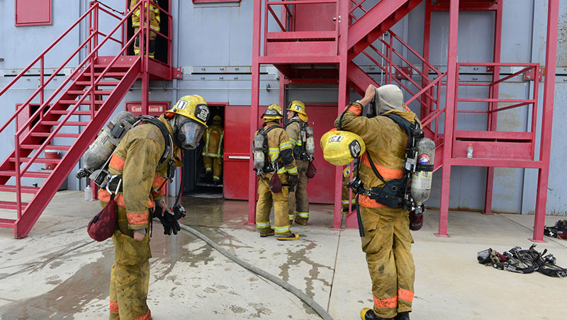 Fire cadets in fire protection suits conduct a rescue simulation