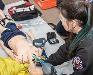 An EMT cadet holds a breathing bag to the face of a medical dummy