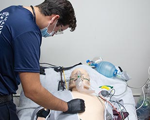 An EMT cadet stands over a medical dummy during simulations