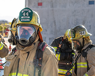 A student in a firefighter uniform and mask looks at the camera