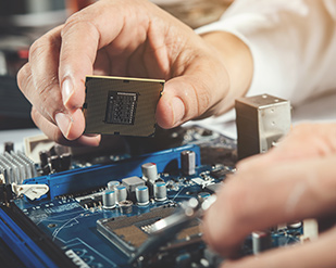 A technician works on a computer motherboard while holding a CPU chip