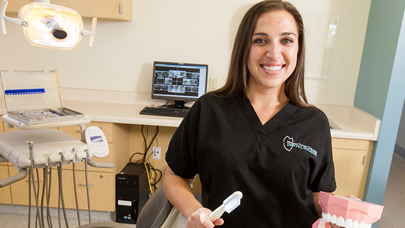 A dental hygiene student poses in front of dental equipment