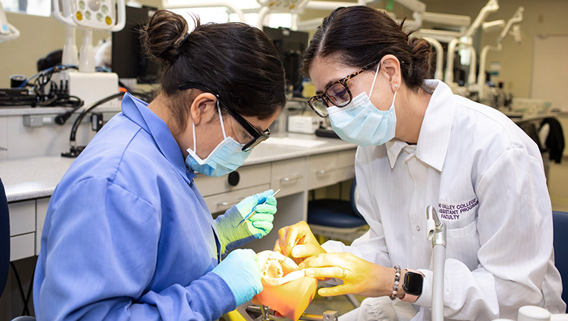 A dental assisting student and faculty member practice cleaning techniques