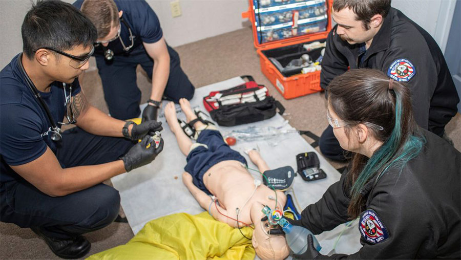 Three emergency medical services students conduct medical safety drills on a dummy