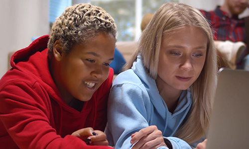 Two female students study together on a single laptop