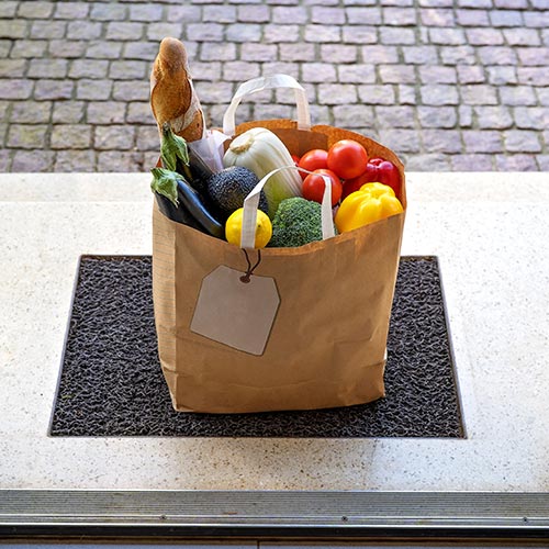 A delivered paper grocery bag of fresh produce on a doorstep
