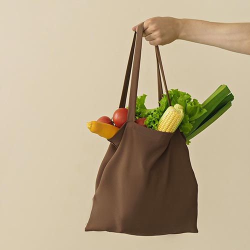 A man holds out a brown canvas bag of fresh produce